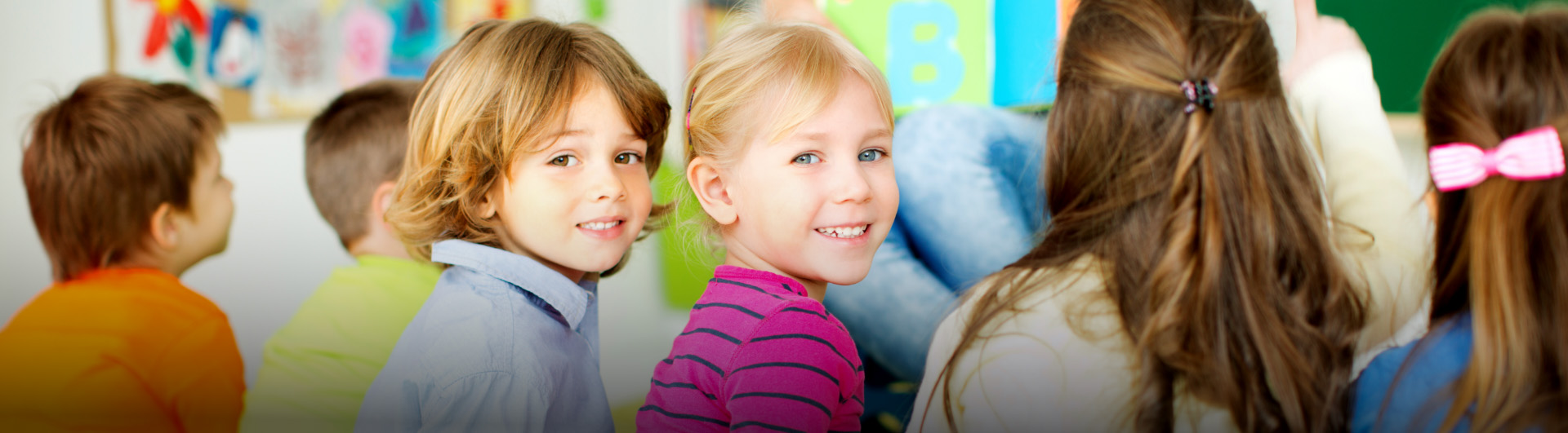 Two children in classroom turning heads to look at viewer